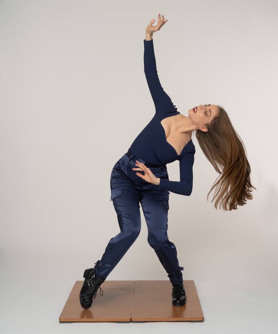 Hillary-Marie in a navy outfit and black tap shoes on a wooden tap board, leaning back with one arm reaching up and her hair flying